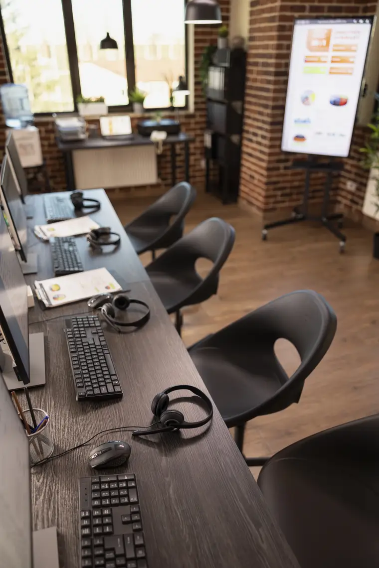 Modern office workspace with computers, headsets and a presentation screen