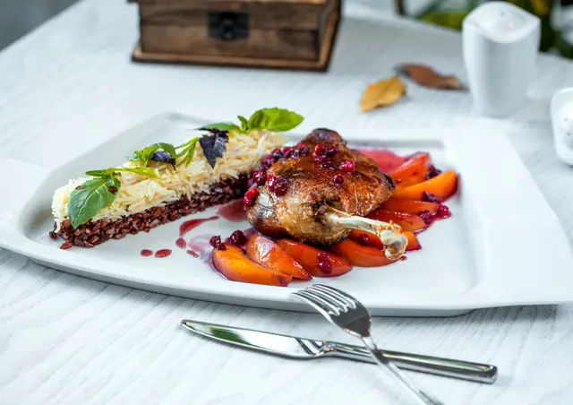 Plated dish with rice, roasted meat and fruit on a restaurant table