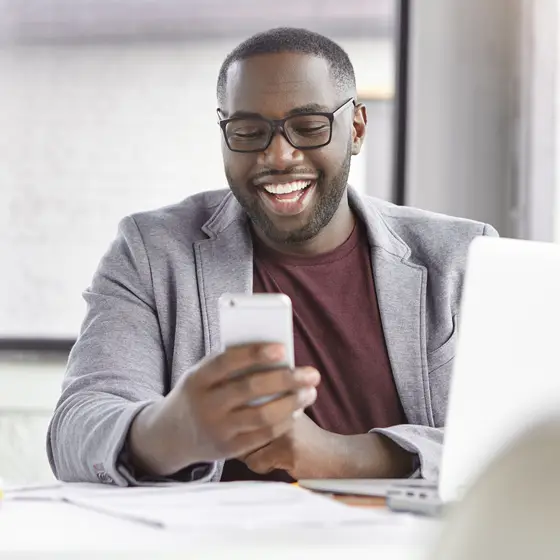 Smiling business owner checking his phone at a laptop